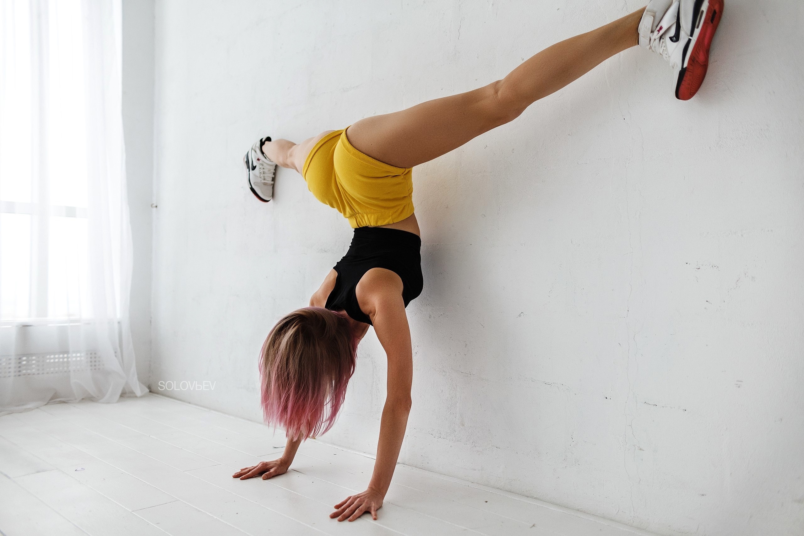 Стройная гимнастка в красном боди делает растяжку в зале на полу